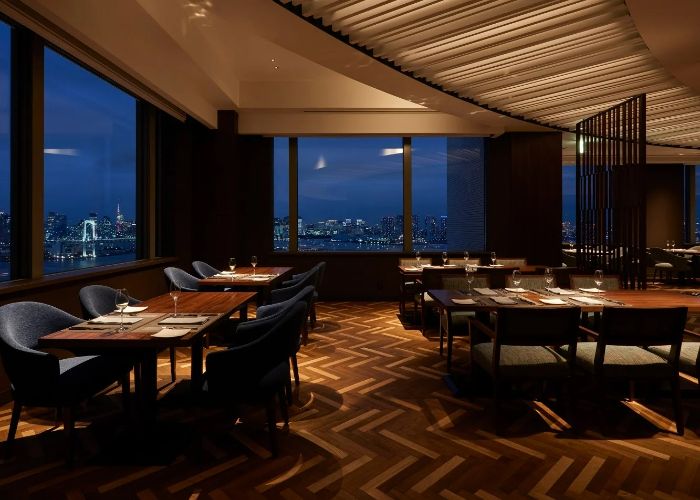The stylish interiors of The Grill on 30th, featuring dark woods, low lighting, and views over Tokyo.